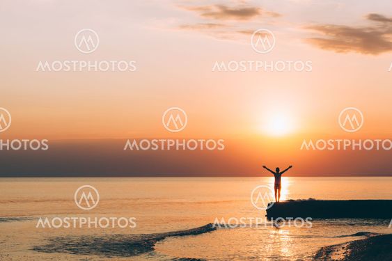 Young woman standing with raised arms in sunset