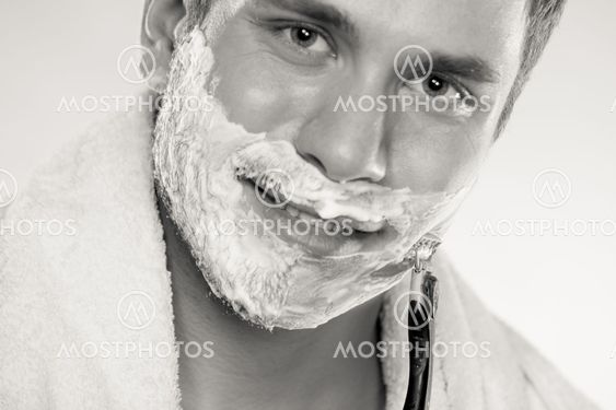 Young man shaving using razor with cream foam.