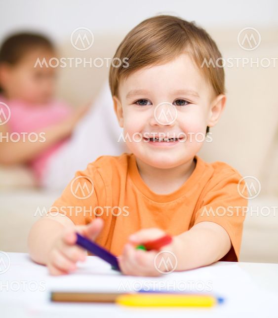 Little boy is drawing on white paper