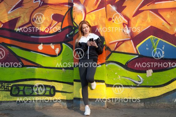 Runner girl resting with mobile phone against bright graffiti wall
