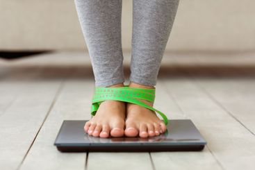 Woman Standing On Weight-Scales, With Measuring Tape On...