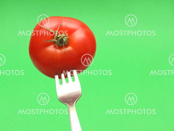 fresh tomato on fork with green background