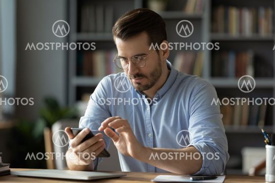 Serious businessman wearing spectacles using mobile...
