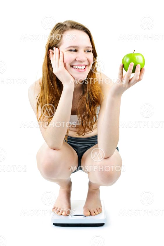 Young smiling girl on bathroom scale holding apple