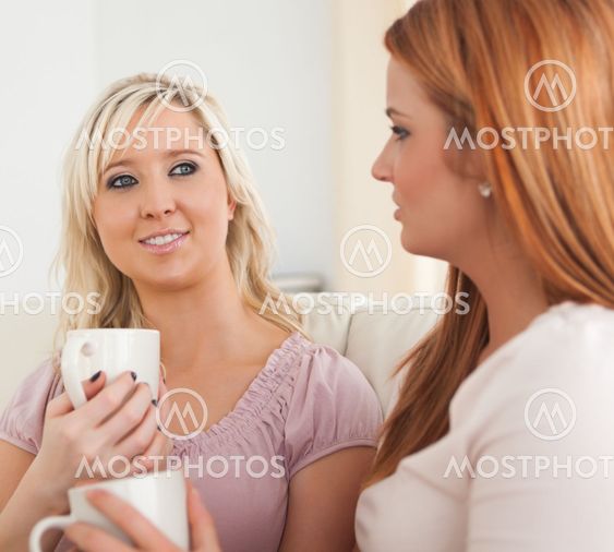 Cute Young Women sitting on a sofa with cups