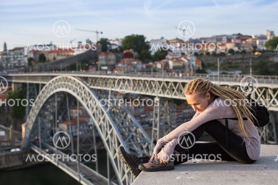 Young beautiful woman with dreadlocks sitting on the background of the bridge of Dom Luis I, Porto, Portugal.