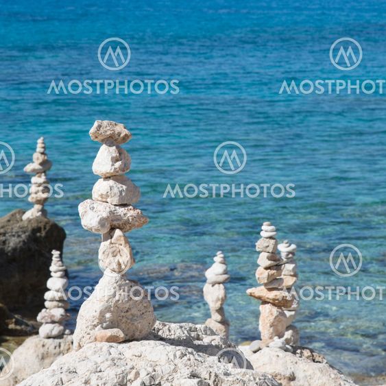 Pebbles and stones stacked on a rock seashore for a blue background with water