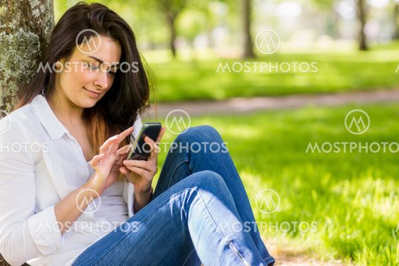 Beautiful brunette sending text in the park