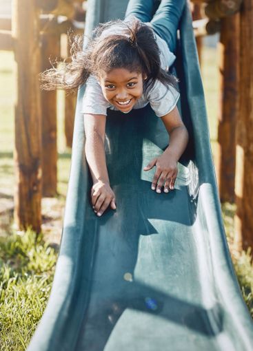 Slide, playing and portrait of child in park for fun,...