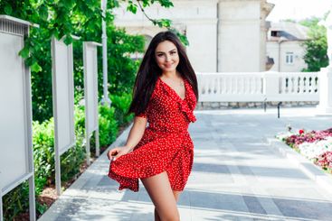 Beautiful brunette woman in a red summer dress walking...