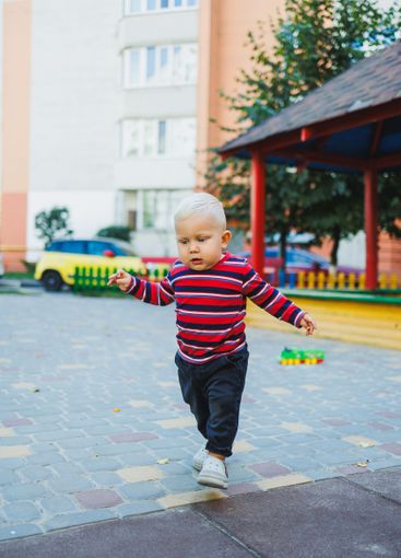 A fair-haired one-year-old boy in jeans and sneakers...