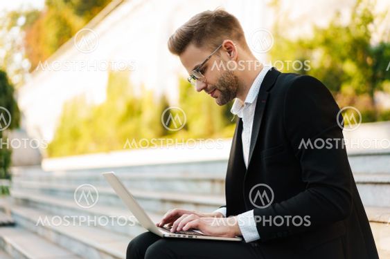 Handsome focused businessman working with laptop while...
