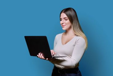 Young smiling woman using laptop on blue studio background