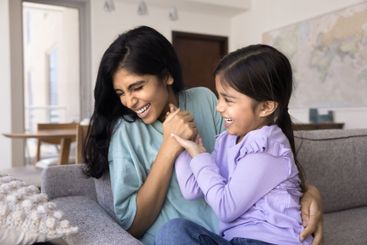 Lovely little girl and young mother playing seated on sofa