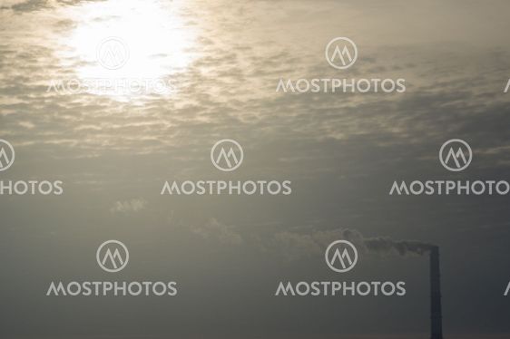 Steam from smokestack against morning sun and clouds