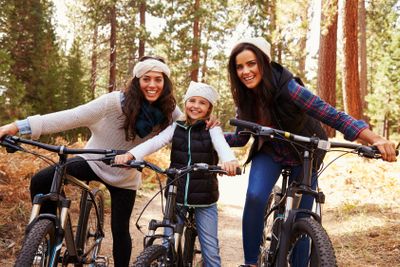 Female parents cycling with their daughter in a forest