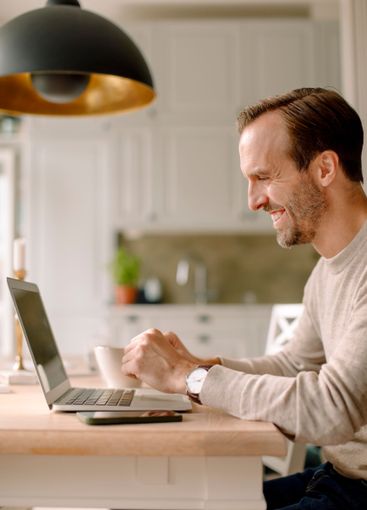 Side view of smiling businessman using laptop in kitchen...