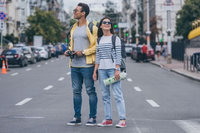 Woman holding map and standing on road near bi-racial...