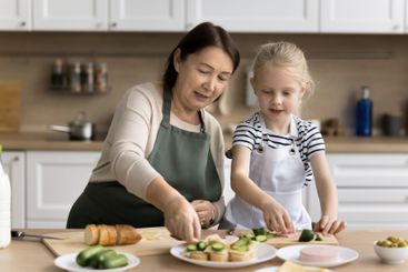 Grandmother and granddaughter preparing food together in...