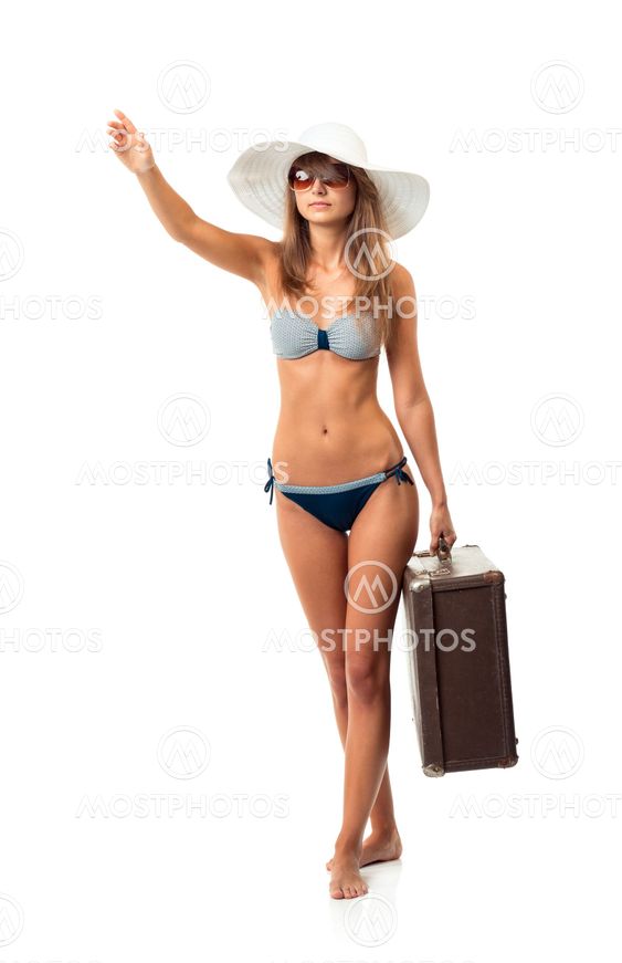 Full length portrait of a beautiful young woman posing in a bikini, hat and sunglasses with a suitcase in hand on white