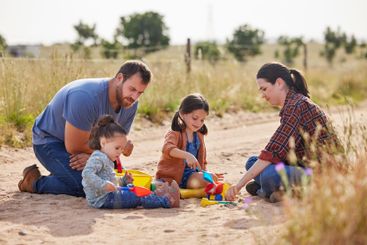 Parents, children and playing with toys in sand for...