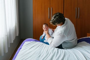 Mother holding her one month old baby son on bed, baby...