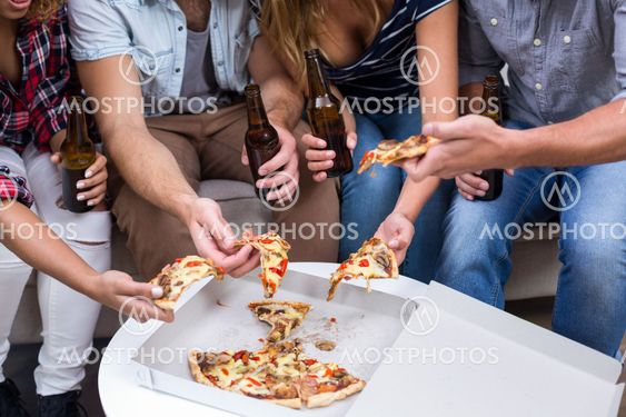 Friends holding beer while eating pizza at home