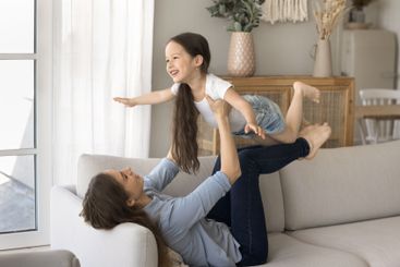 Mom support little daughter in air with legs play flying