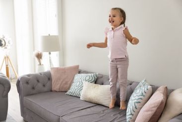 Excited sweet little preschool girl jumping on home sofa