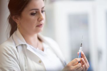 A focused nurse in a white lab coat carefully prepares a...