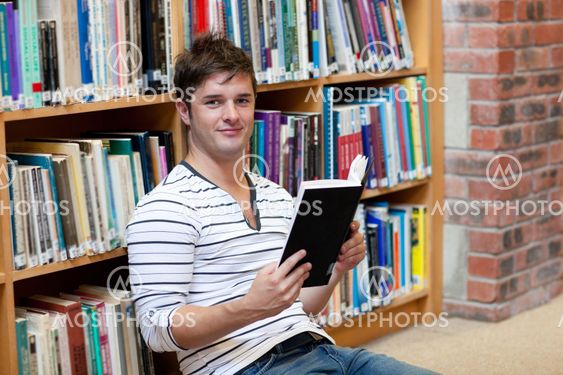 Handsome male student reading a book sitting on the floor