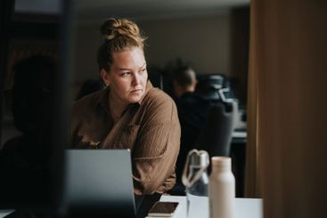 Thoughtful businesswoman sitting with laptop near desk at...