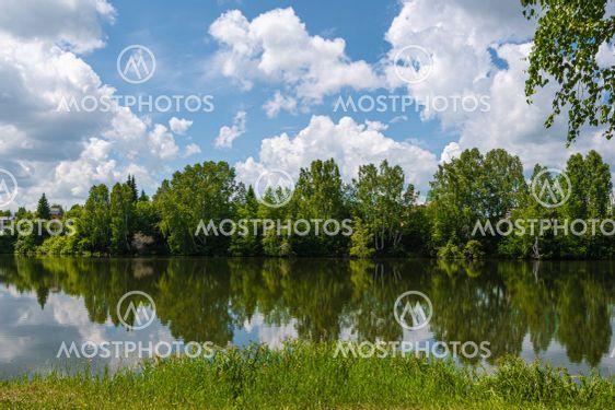 Reflection of green trees and blue sky with clouds in...