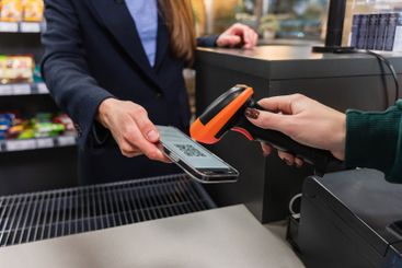 A cashier scans a qr code from a smart phone using a...