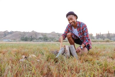 Smiling african man sitting and making campfire outdoors
