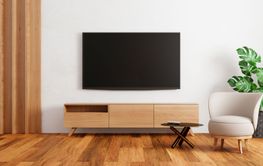 TV above wooden cabinet in modern empty room with plants...