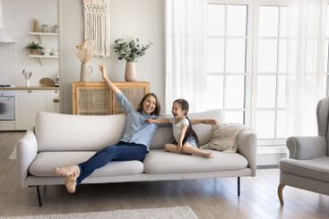 Excited mom little daughter rest on sofa at comfortable...