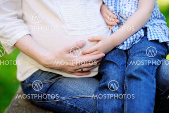Mother's and daughter's hands on a pregnant belly