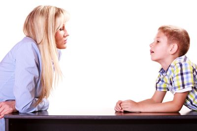 Mother and son talk and argue sit at table.