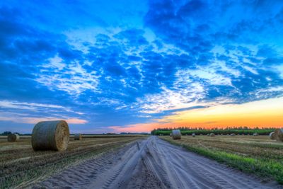 Sunset over rural road and hay bales