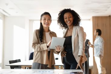 Two happy diverse female business partners posing in...