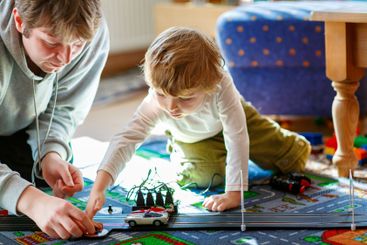 Father and son playing with racing cars on racetrack,...