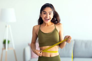 Portrait of young Indian woman measuring her waist with...