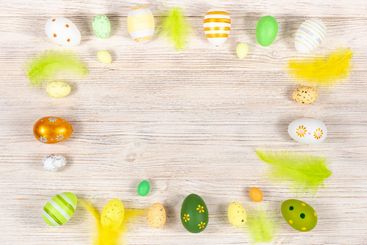 Easter frame with eggs and feathers on a light wooden...