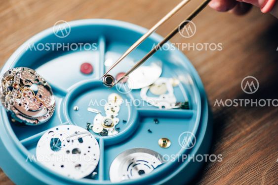 Cropped view of watchmaker holding watchpart in tweezers...