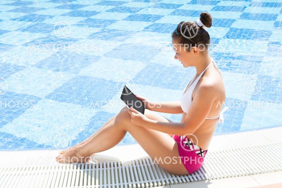 Woman Using Digital Tablet At The Edge Of Swimming Pool