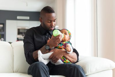 Young african american father giving milk to  her baby...