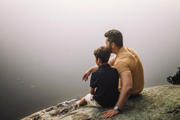 Father sitting with son on rock near lake
