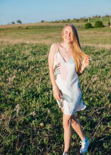 blonde woman in summer dress walking in blooming grass...