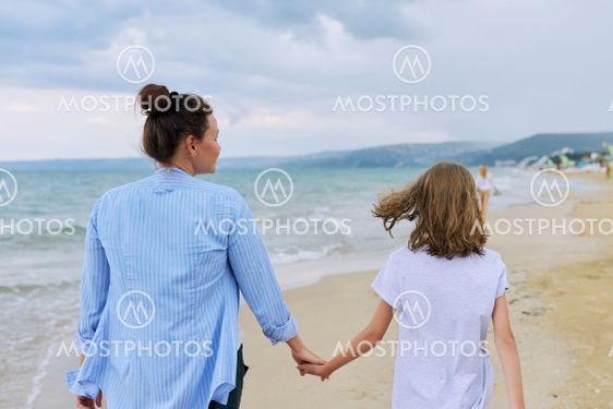 Happy mom and daughter walking on the sea beach holding...